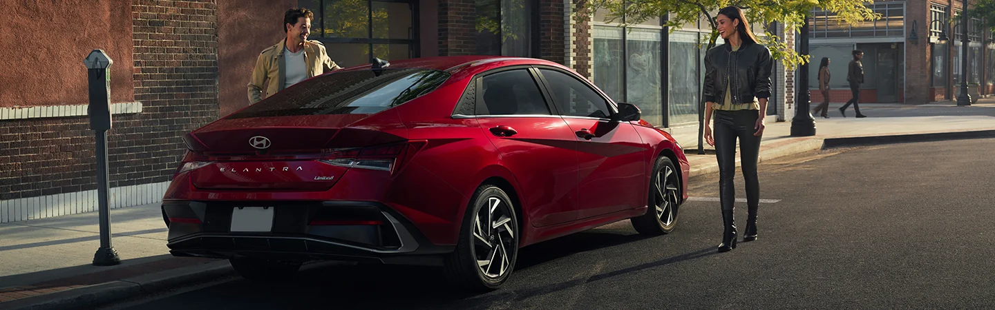 2025 Hyundai Elantra vs Toyota Corolla red color A man and women is standing on the road and looking at a car