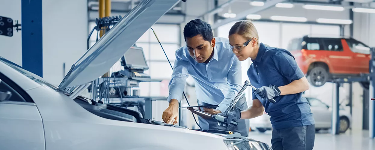 Two service mechanics working under the hood of a vehicle
