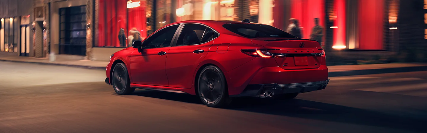 Back side view of a red 2026 Toyota Camry driving though the city