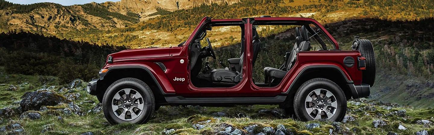 Side view of a red, four-door 2021 Jeep Wrangler without its doors parked on rocky terrain in the mountains.