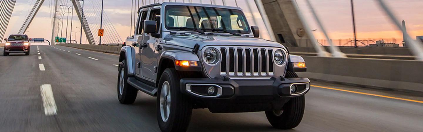 Front view of a silver 2021 Jeep Wrangler driving over a bridge.