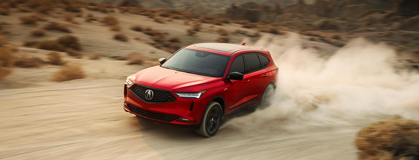 Front view of a red Acura MDX driving a dirt road