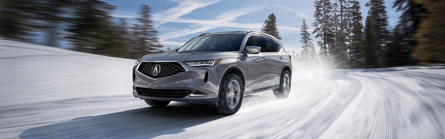 Side profile of a silver Acura MDX driving in the snow