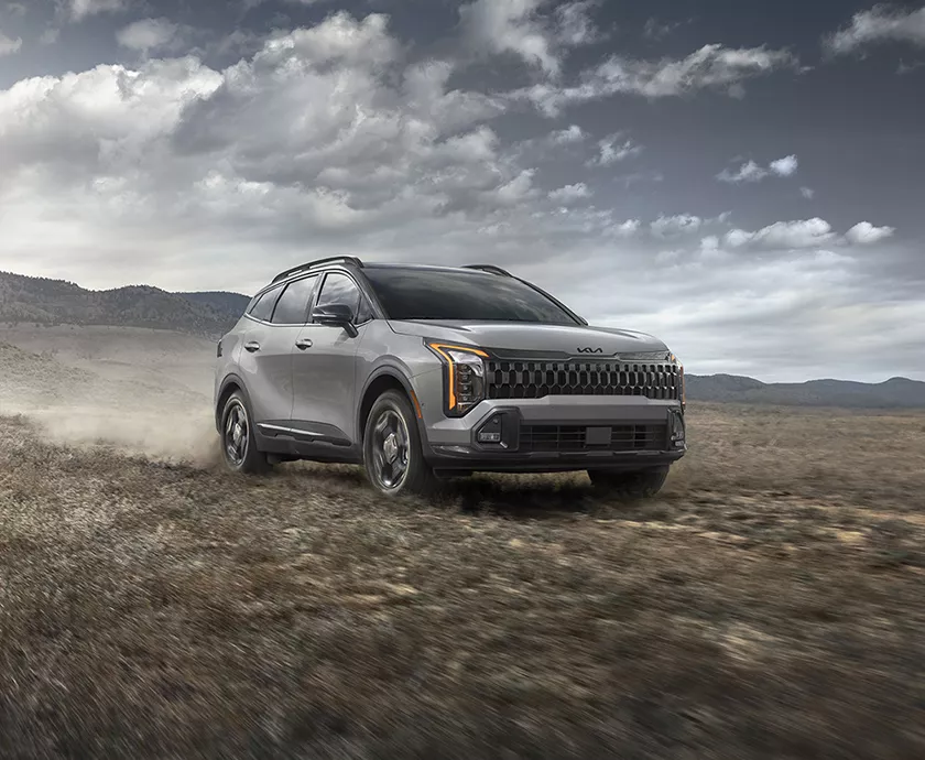 2026 Kia Sportage driving in a grass field with mountains in the background