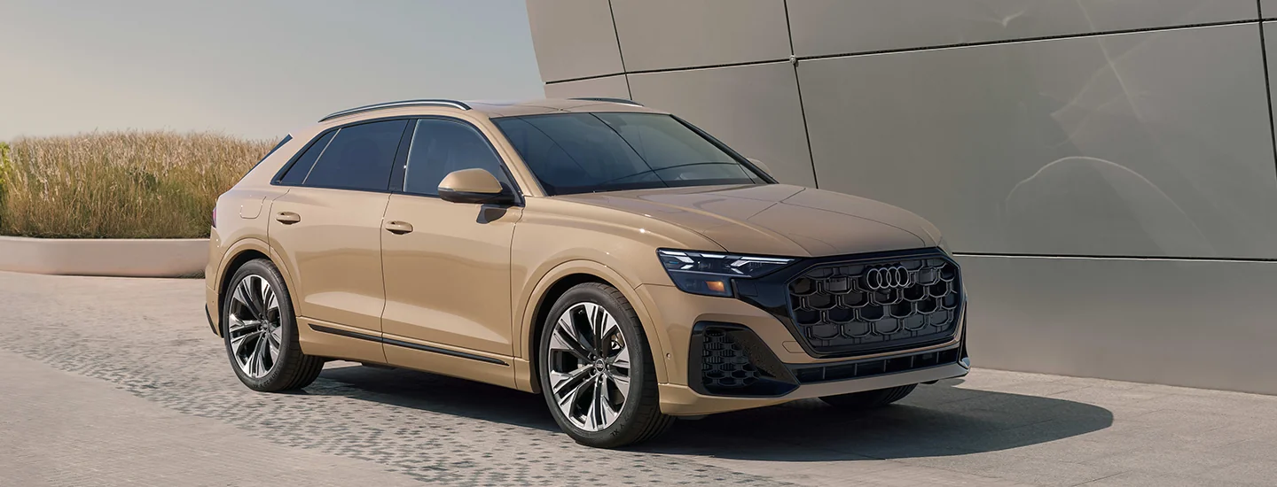 Front side view of a parked tan 2025 Audi Q8 next to a building