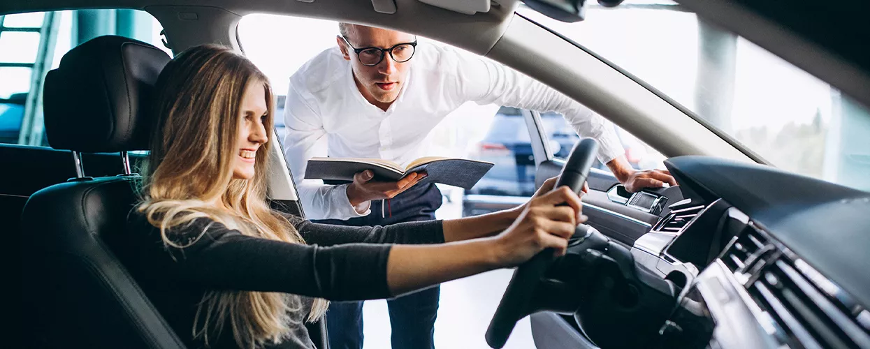 Woman siting in a vehicle in a car dealership with a car salesman standing outside