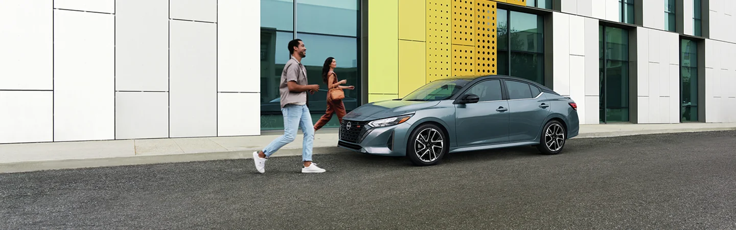 The 2025 Nissan Sentra in St. Petersburg, FL gray color car stand on city men and women are running on the road and looking at the car