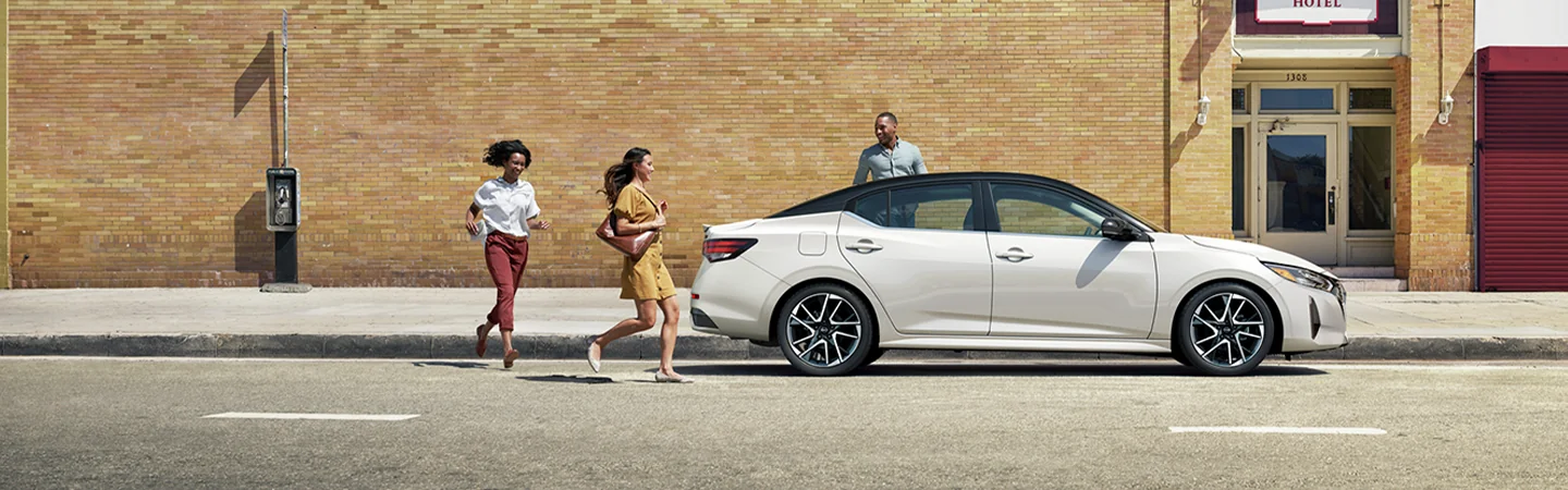 The 2025 Nissan Sentra in St. Petersburg, FL white color car stand on city womens are running on the road and looking at the car 