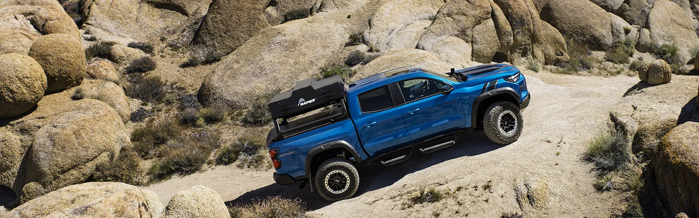 Side view of a blue 2025 Chevrolet Colorado driving on rocks