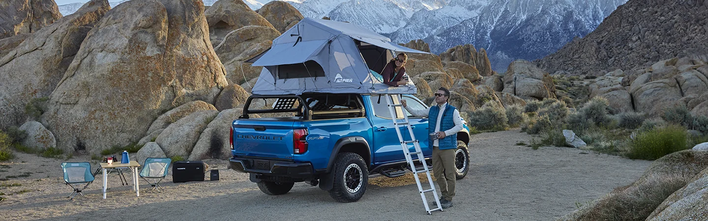 Parked blue 2025 Chevrolet Colorado with a tent on top with a family camping