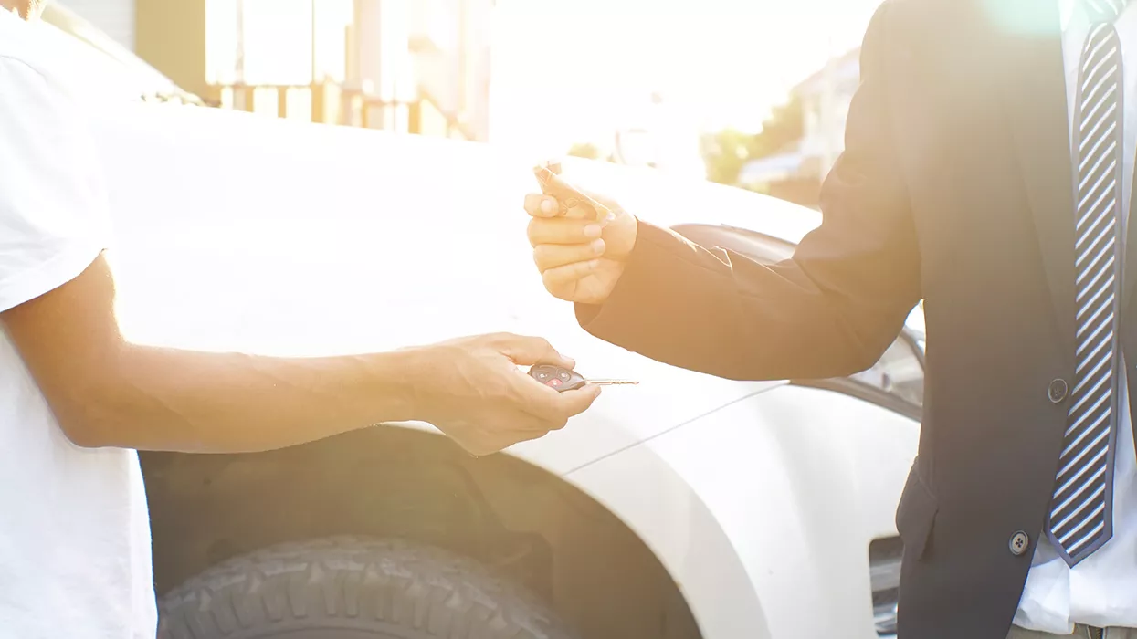 Someone being handed keys with a car in the background