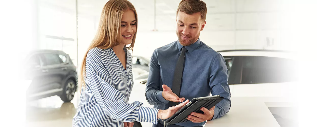 Customer and car salesman looking at a tablet in a car dealership