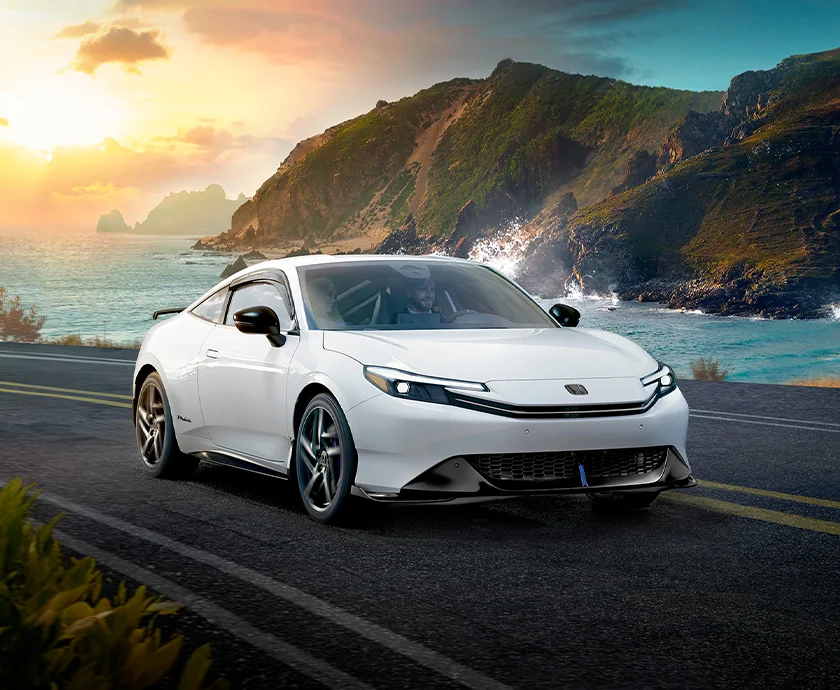 Front view of a white 2026 Honda Prelude driving on a road next to the ocean