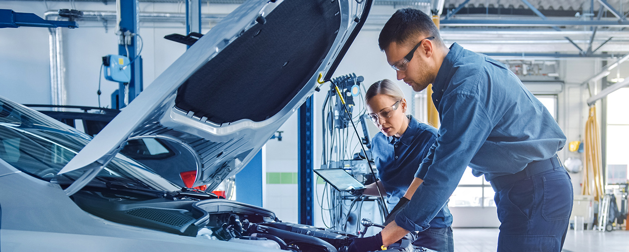 Two people repairing a car in a garage, focused on their work with tools and parts scattered around them.