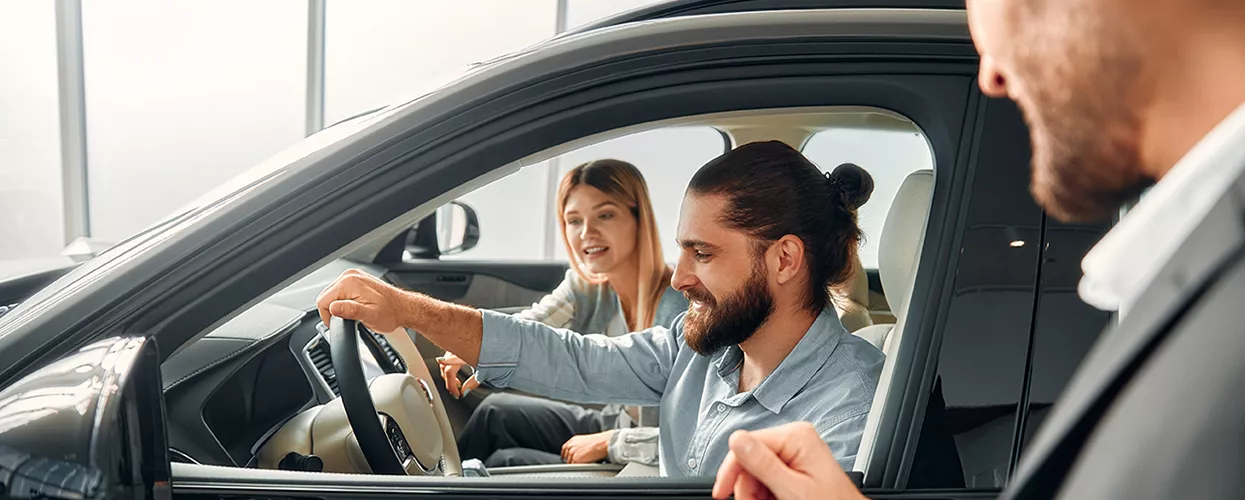 A couple sitting inside of a new car in a car dealership