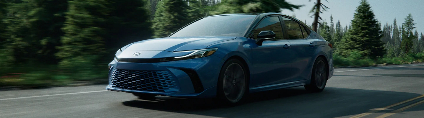 Blue Toyota drving on a road by some woods