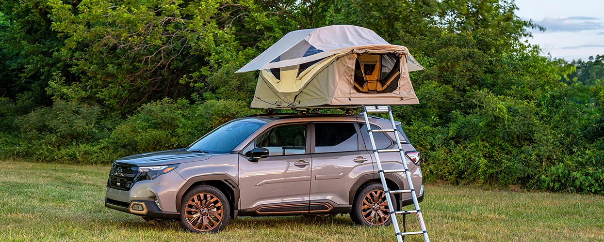 a 2026 Subaru Outback parked outdoors with a tent mounted on its roof, ready for camping adventures.