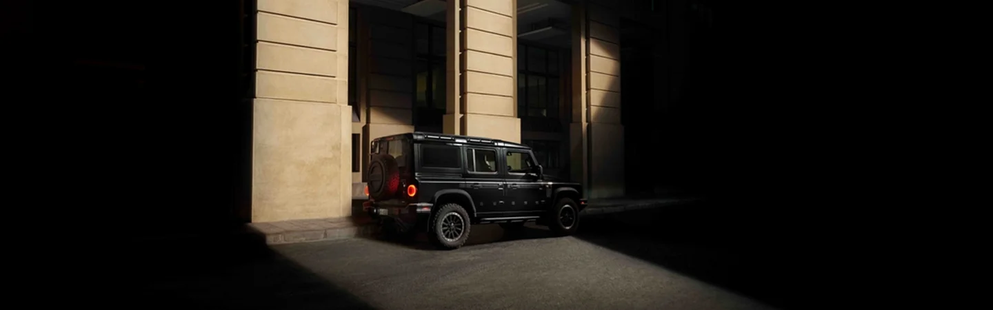 Side view of a black 2025 INEOS Grenadier Trialmaster driving in the city