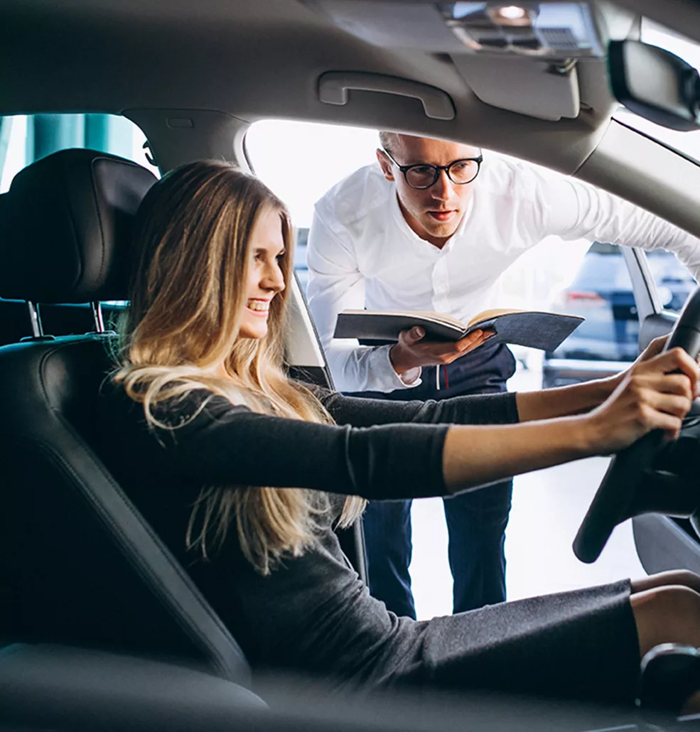 Woman sitting in a new vehicle with a car salesman talking to her