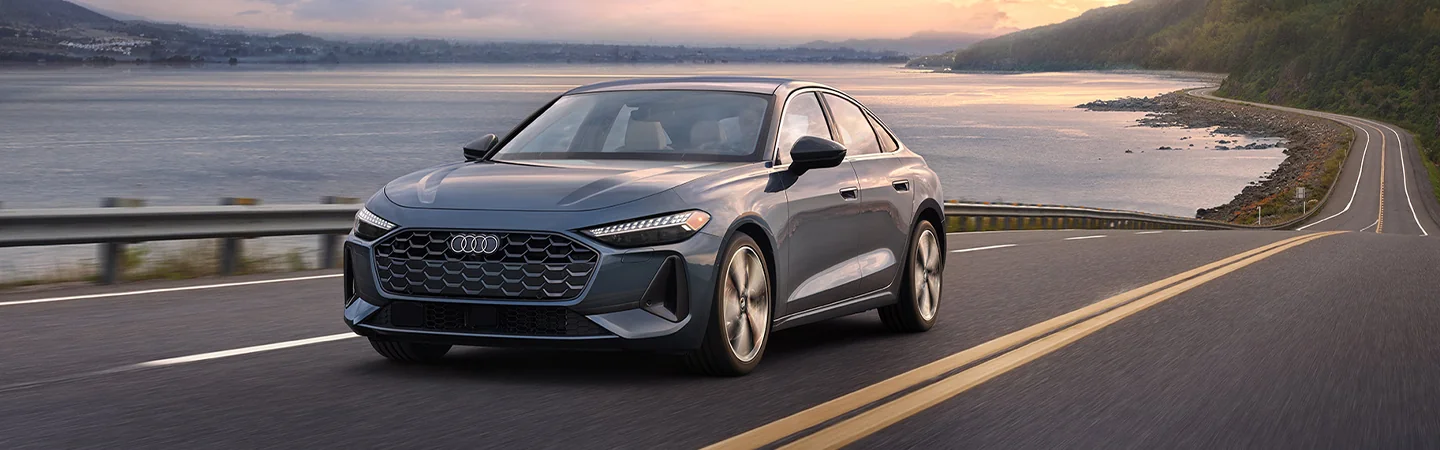 Gray 2025 Audi A5 driving on a road next to some water