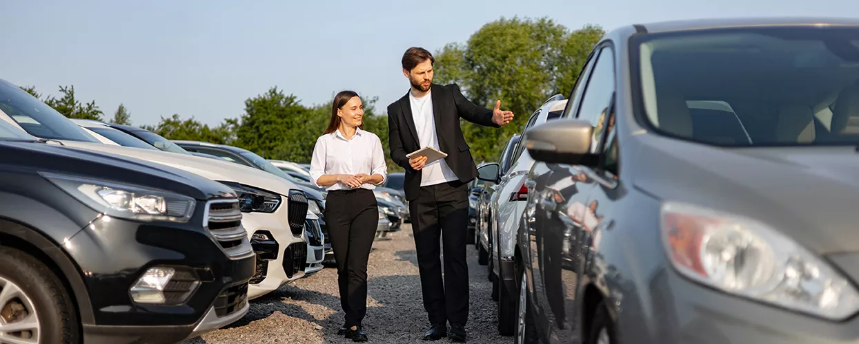 Two people looking at a pre-owned Mazda vehicle on a dealership lot