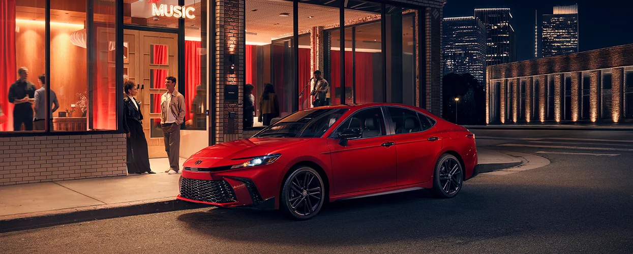a red 2026 Toyota Camry Hybrid parked by a diner in a city