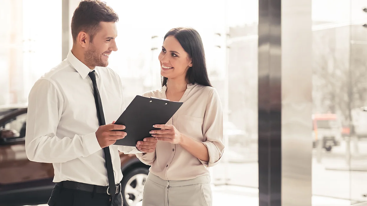 car salesperson speaking with customer in showroom smiling over details of car lease