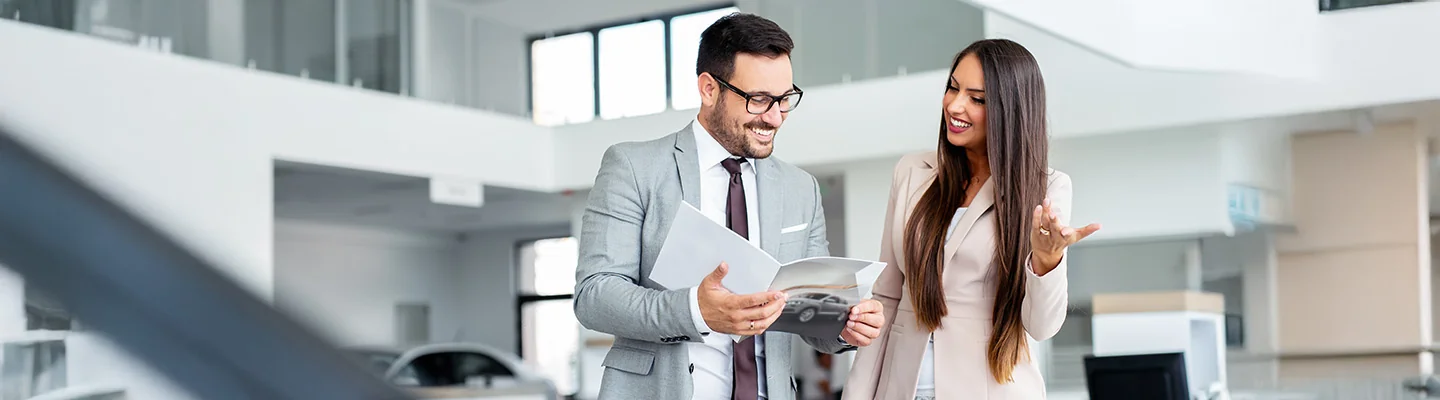 two people discussing specifications of a new car in dealer showroom