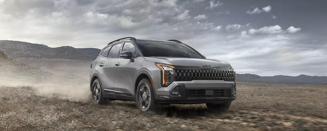 2026 Kia Sportage driving on a dirt path with mountains behind it