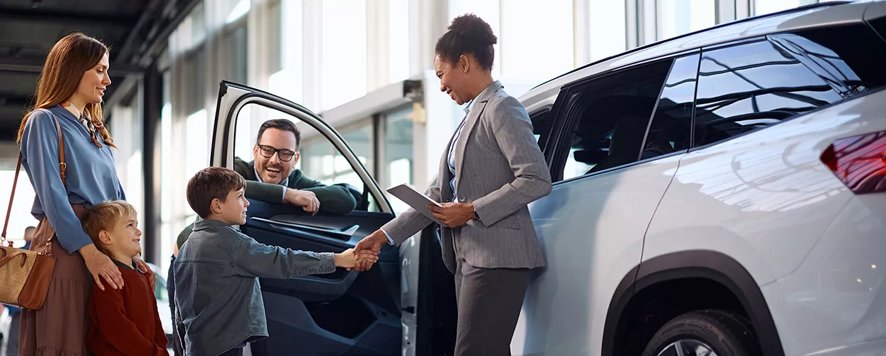 Family shaking hands with a car saleswoman in a car dealership
