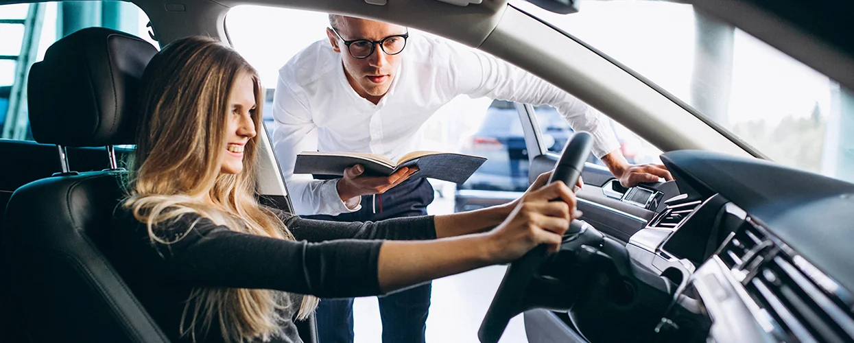 A man and woman are seated in a car, looking intently at a book they are sharing.