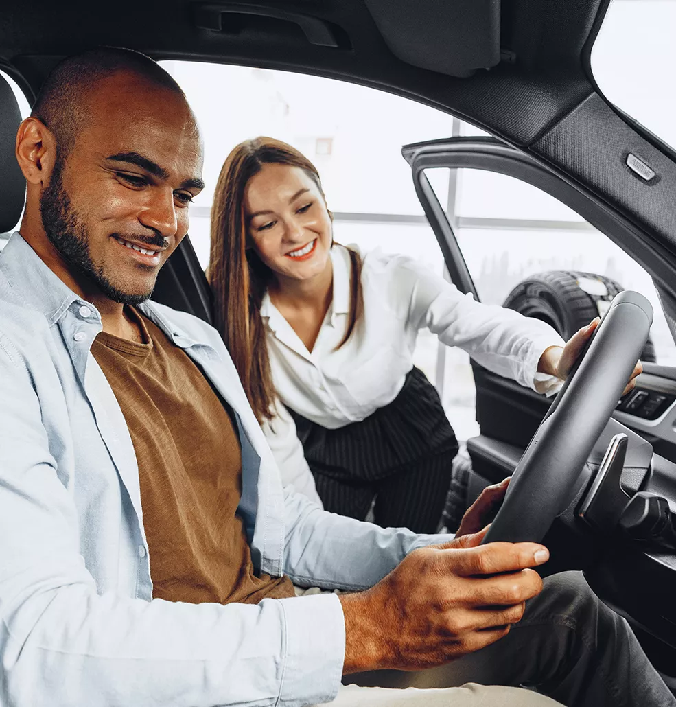 A customer sitting in a new Subaru with a saleswomen smiling