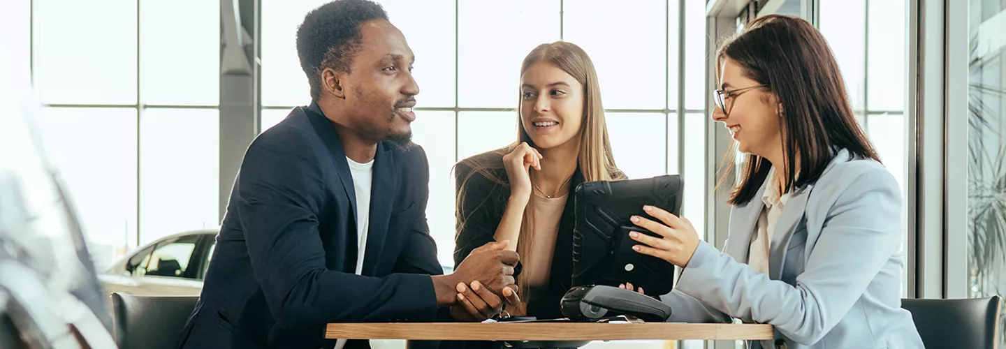Two people talking to a car saleswoman at a table