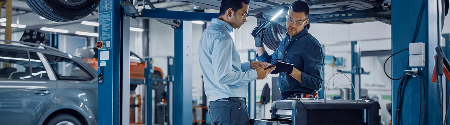 mechanic and tech working under a vehicle looking at a report