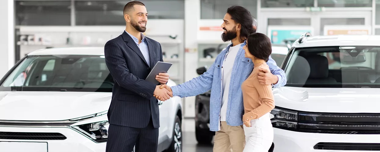 Car salesman shaking hands with a couple in a car dealership