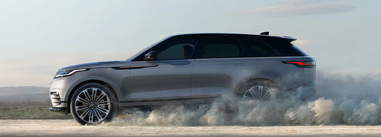 side view of a silver Range Rover Velar kicking up some dust in motion