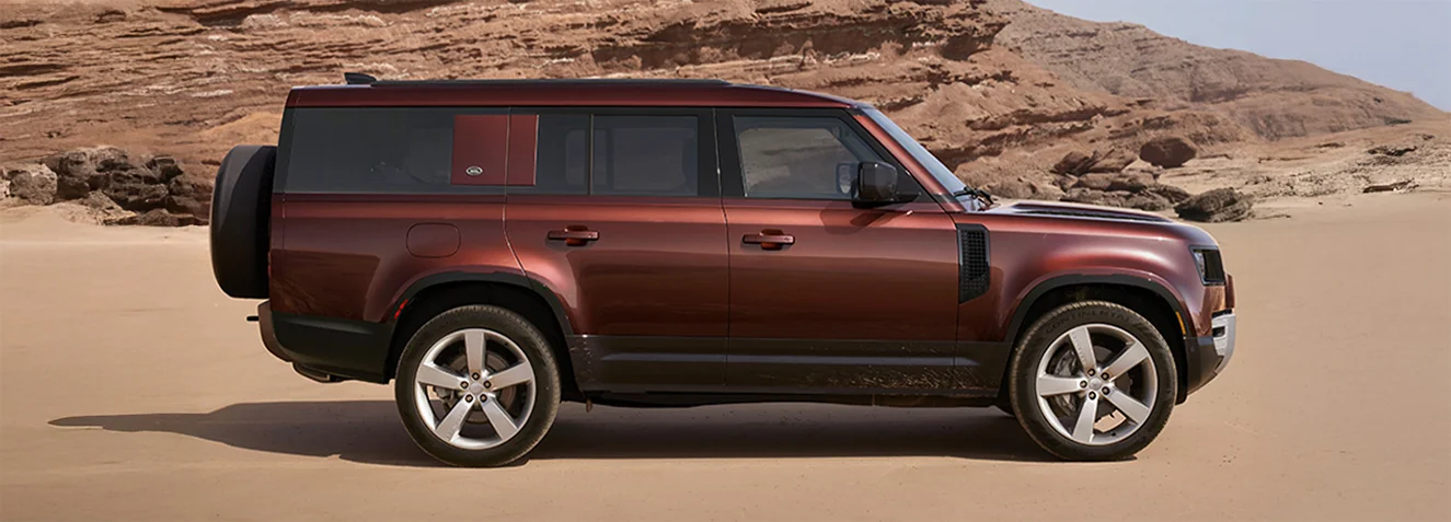side view of a rust colored Defender 110 in a desert