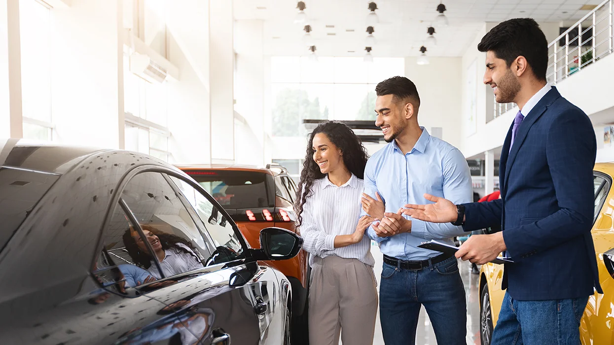 couple with car salesperson in showroom lookng at cars for sale