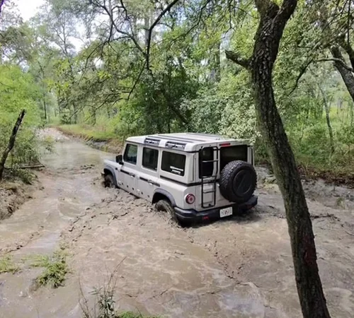 Back view of a white INEOS Grenadier driving though a river