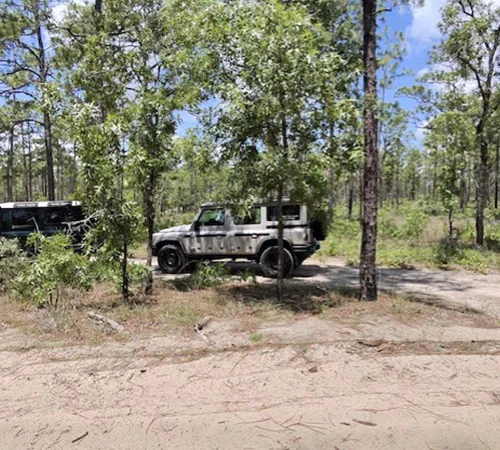Two INEOS Grenadier driving behind some trees in the mud