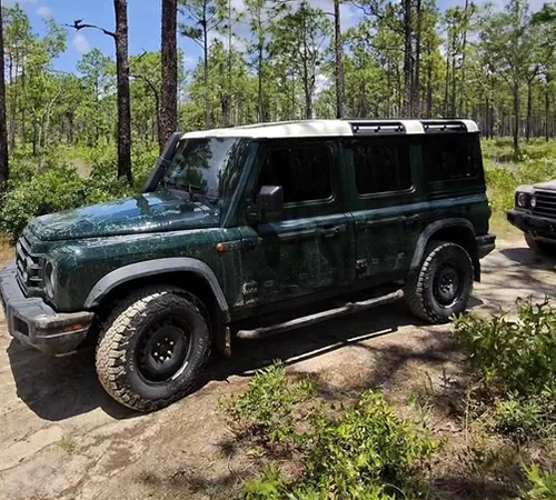 Side view of a green INEOS Grenadier parked in the woods