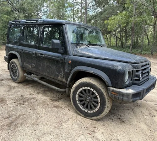 Close up front side view of parked green INEOS Grenadier in the woods