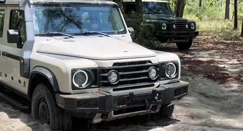Close up of a white and green INEOS Grenadier driving in the woods though some mud
