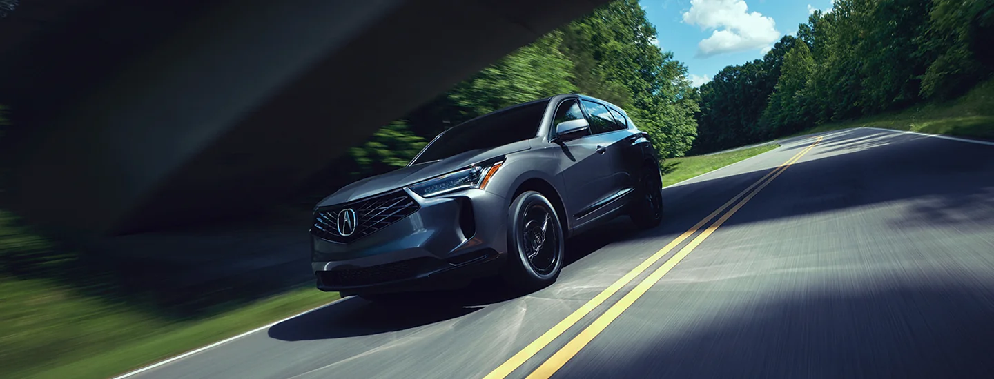 Front view of a 2025 Acura RDX driving on a road by woods