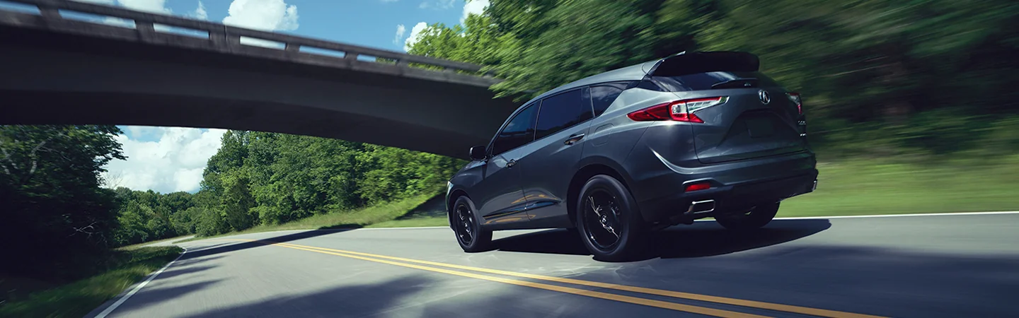 Back view of a 2025 Acura RDX drivng on a road by woods