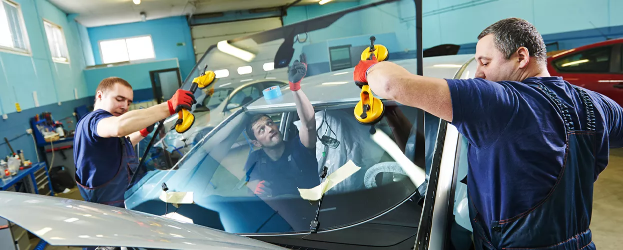 Automotive technicians replacing a vehicle windshield in a professional auto glass repair and installation center
