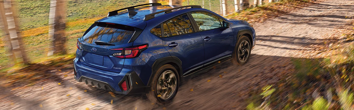 dark blue rear top view of 2025 Subaru Crosstrek Wilderness in motion driving on dirt road