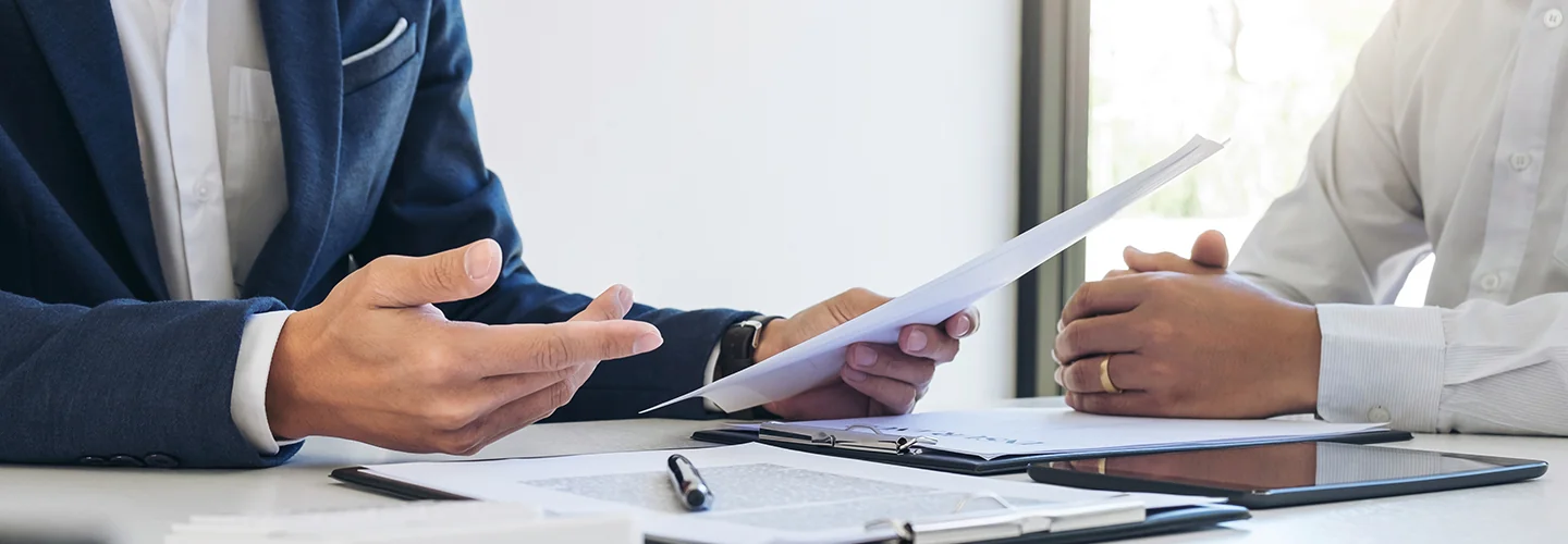person holding papers aroung a desk with another person