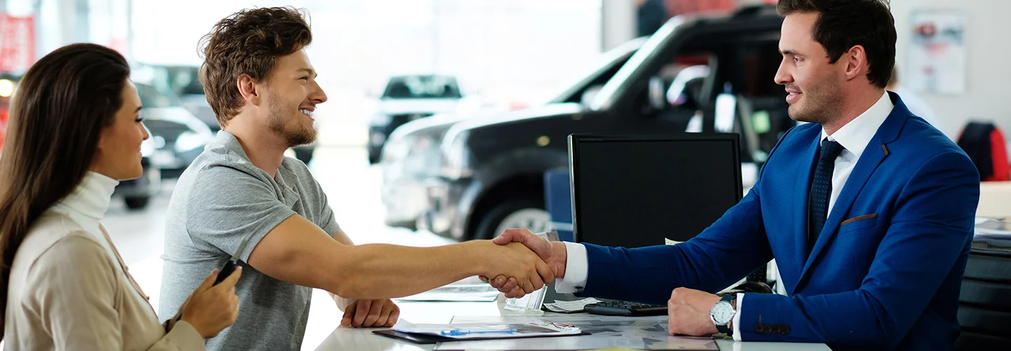 Sales person shaking hands with customers after closing on there new car