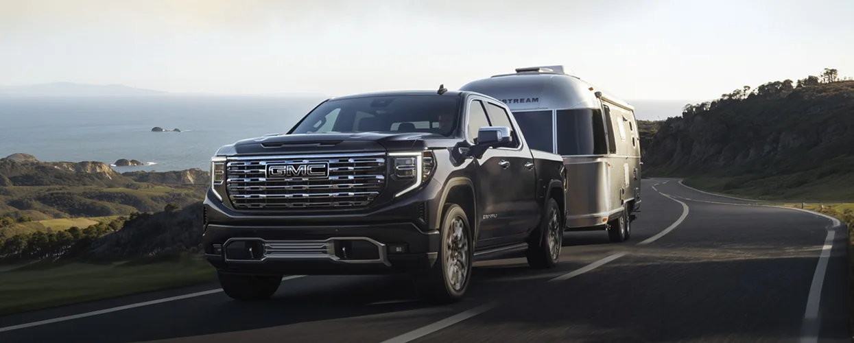 a 2026 GMC Sierra 1500 towing a camper trailer on a scenic road, showcasing its powerful towing capability.